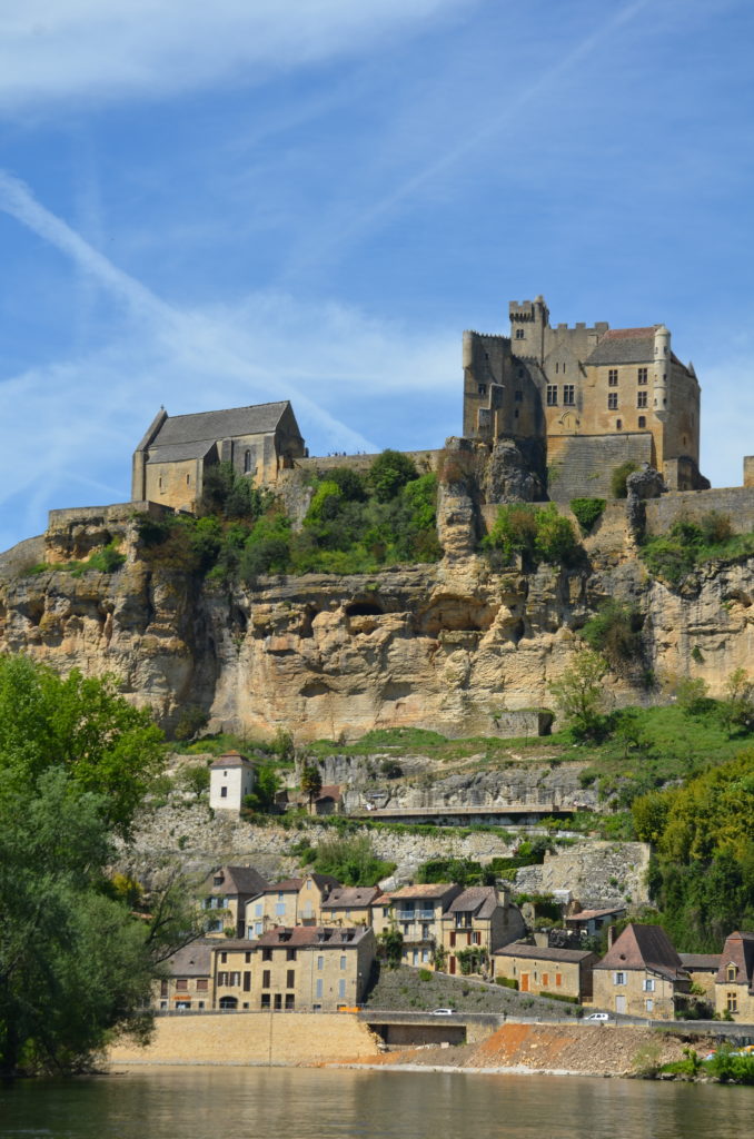 View on Beynac from the river while on the gabarre. Castle on top and walls and houses along the mountain.