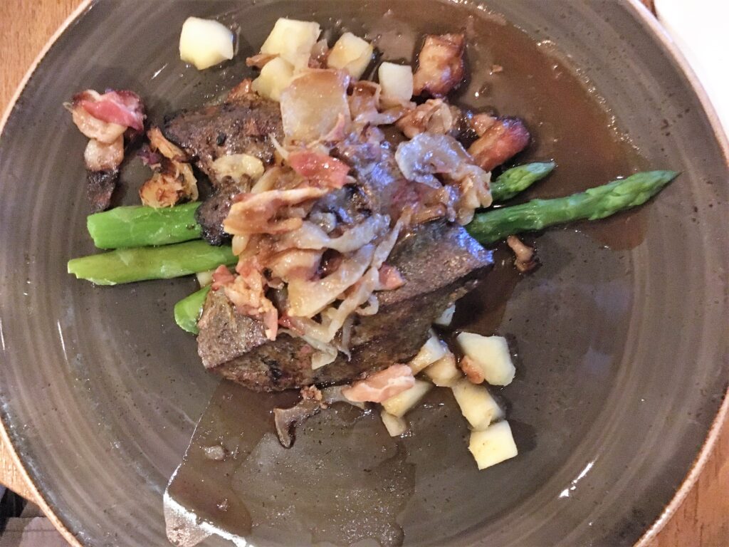 Veal liver with green asparagus under it and bacon over it.
