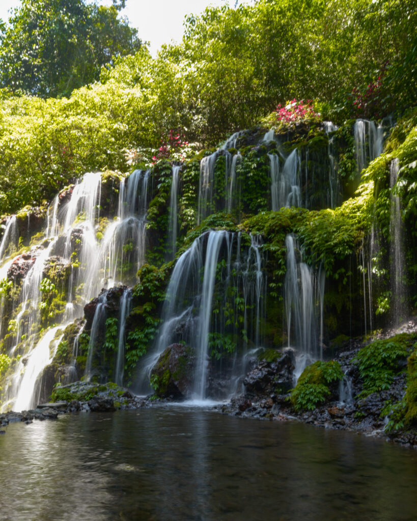 Banyu Wana Amertha Waterfall, several streams flowing down over lush green rocks.