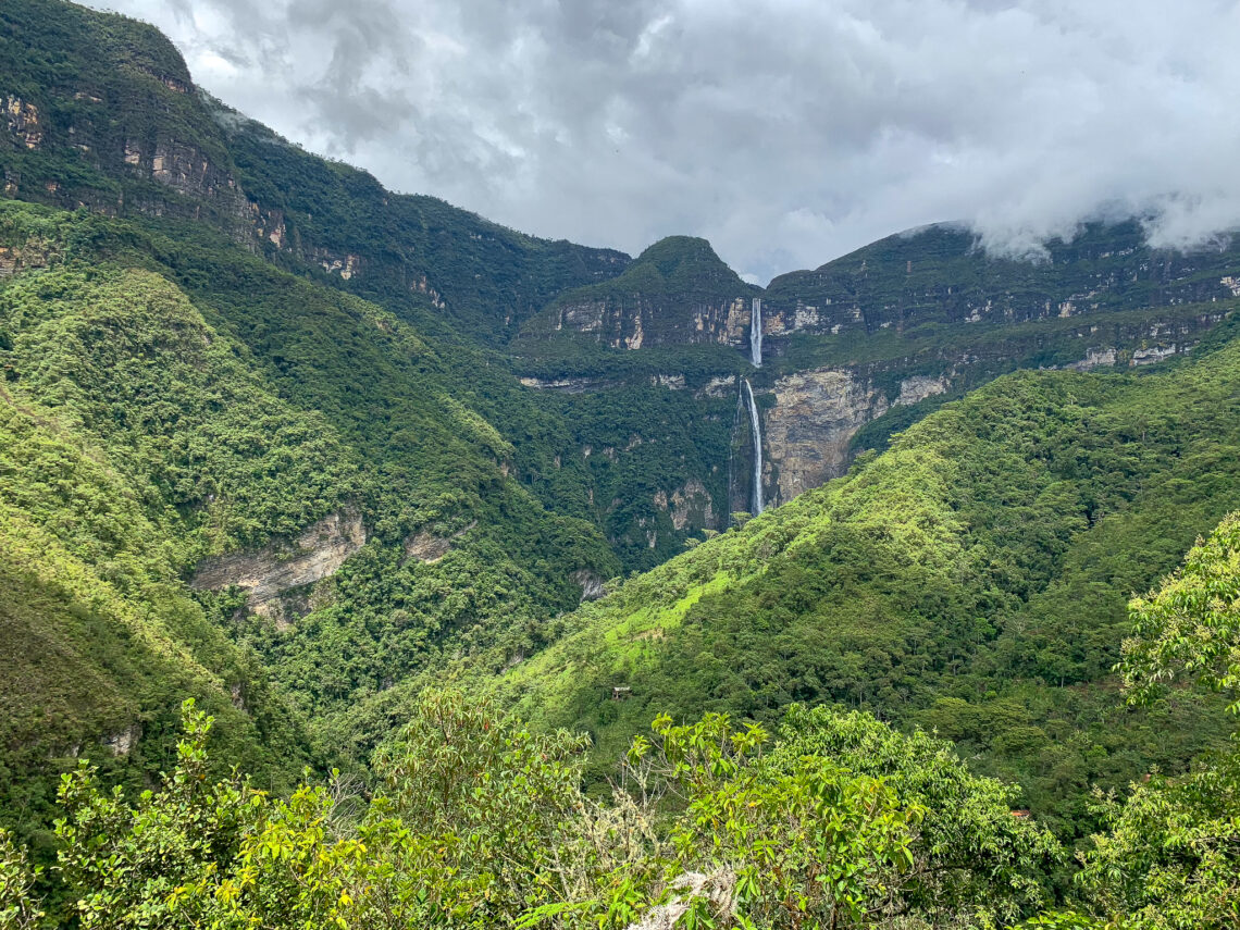 Gocta Falls from a distance, in between green mountains, with an overcast sky