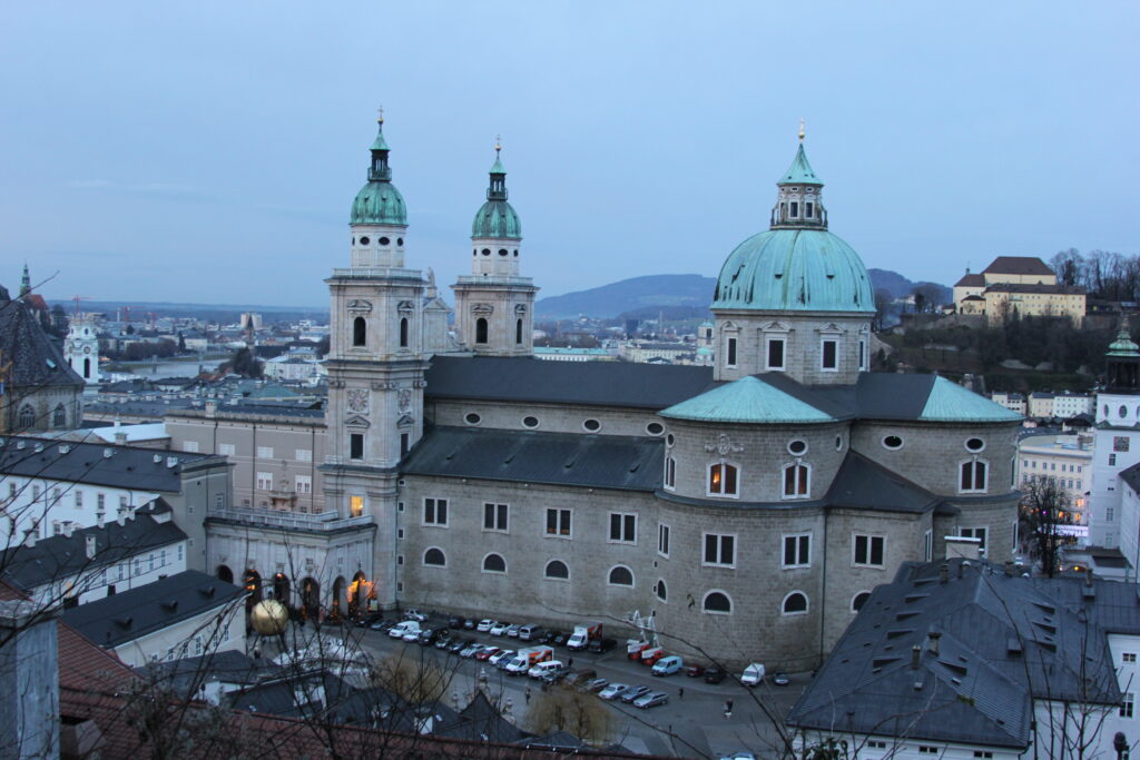 Salzburg by Paula Pins the Planet, a clowded view on Salzburg , in the middle a large building (church), where a Christmas market is being held