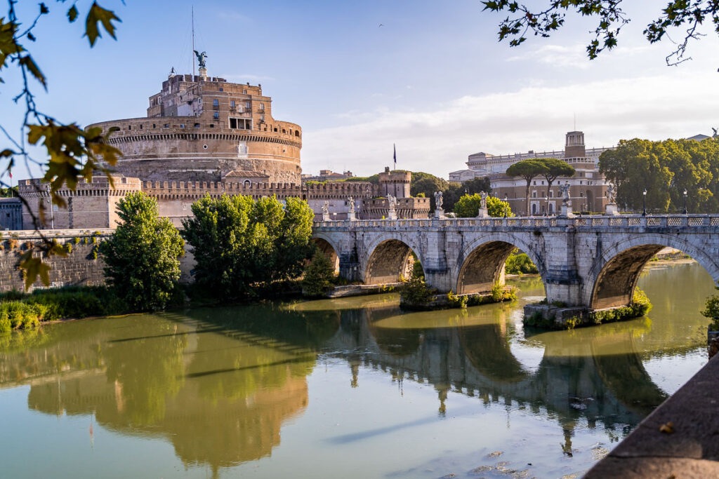 Castel Sant' Angelo, Rome by She Wanders Abroad, a round castle, seen from the other side of the river, , bridge running to it on the right.