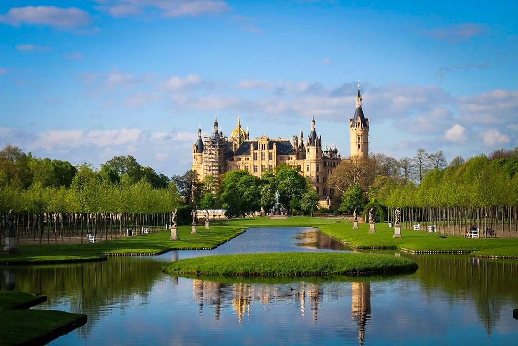 Schwerin Castle by Destination the World, as seen from further away in the gardens. Gardens in front with water and sculptures, grass and trees