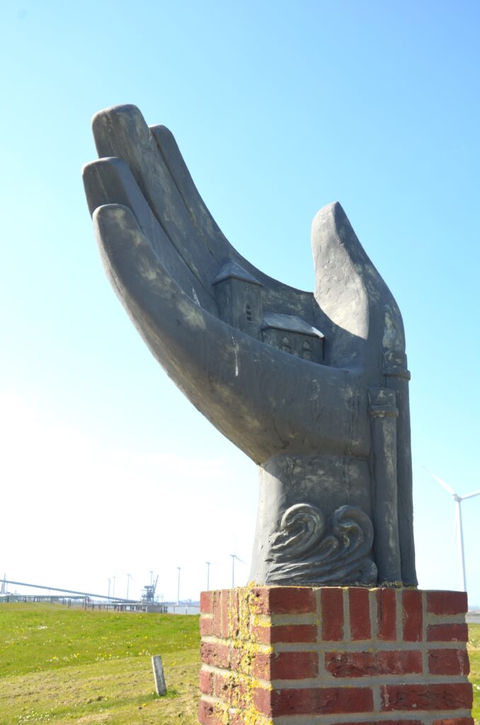 The statue of a hand, a large hand, with waves below on the wrist, two buildings in the palm of the hand